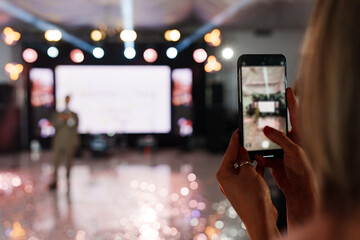 defocus. A woman is filming a man's performance on stage on her smartphone. 