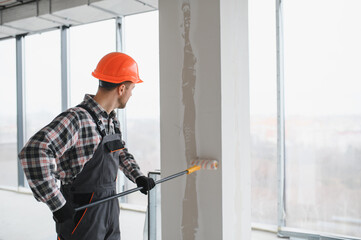 Construction worker painting wall with roller in building under construction