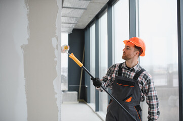Construction worker painting walls with roller in building renovation