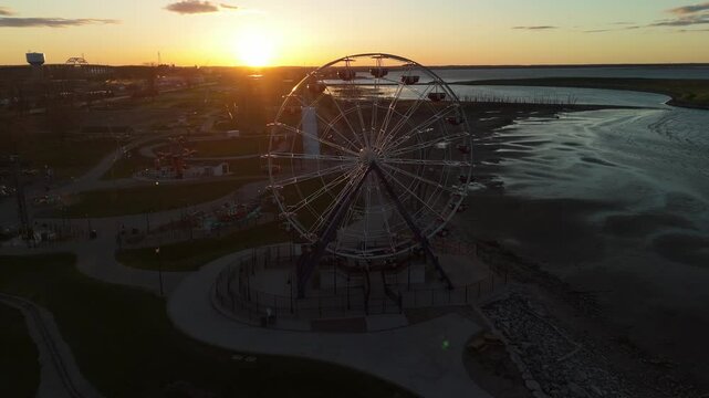 Drone video flying over Bay Beach Amusement Park in Green Bay Wisconsin during sunset featuring roller coaster, Ferris wheel, and glowing sky.