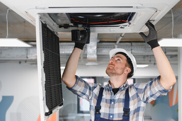 Hvac technician repairing air conditioner unit on ceiling