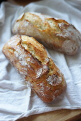 Rustic homemade crusty bread on a white cloth with a slice topped with a piece of butter.