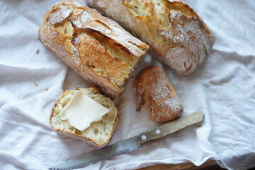 Rustic homemade crusty bread on a white cloth with a slice topped with a piece of butter.