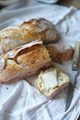 Rustic homemade crusty bread on a white cloth with a slice topped with a piece of butter.