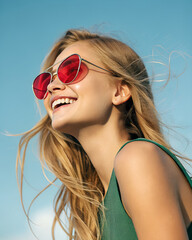 Portrait of a smiling blonde woman wearing red sunglasses against a bright blue sky on a sunny day