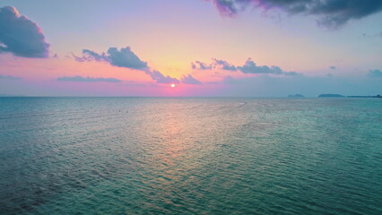 Vibrant sunset colors paint the sky over a tranquil ocean, with the setting sun casting a warm glow...