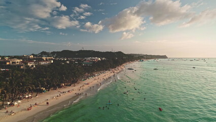 Aerial view of Cagban Beach in Boracay, Philippines during a vibrant sunset, showing tourists swimming, sunbathing, and enjoying watersports activities along the picturesque coastline