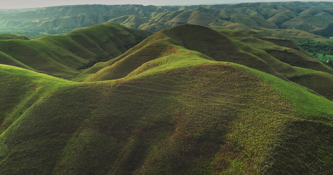 Aerial view of the undulating landscape of Sumba Island, Indonesia, bathed in the warm glow of golden hour, showcasing the beauty of nature's curves and vibrant green vegetation