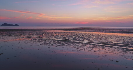 Fototapeta premium Aerial view of beautiful sunset reflecting on the wet sand of a tropical beach at low tide, creating a colorful and serene atmosphere with islands visible on the horizon