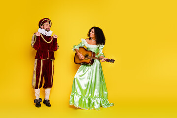 Elegant couple in medieval-inspired costumes posing against a vibrant yellow backdrop in a fun and...