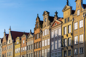 row of colorful historic tenement houses in Gdańsk, illuminated by the warm light of the late afternoon sun. The richly decorated facades and steep roofs create a picturesque view typical of the city'