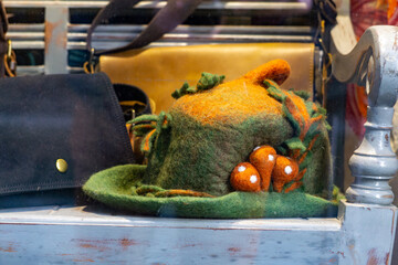 Handmade felt hat in a fantasy style, decorated with mushroom and leaf motifs, displayed in a shop...