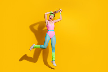 Energetic woman in vibrant retro activewear jumping against yellow background