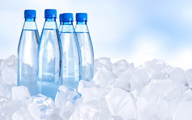 Fototapeta na wymiar Cold water bottles resting on ice cubes on light blue background