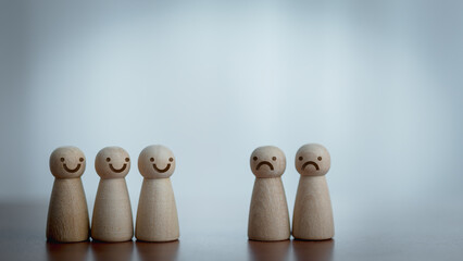 Obraz premium Two groups of wooden figurines showing joy and sadness on wooden table. Concept of emotion, mental health, teamwork, conflict, empathy, and human relationships.