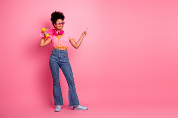 Cheerful girl holding a skateboard against a vibrant pink background with a confident pose and playful gesture