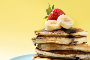 Pancakes with chocolate and fruit on yellow background