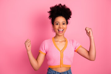 Cheerful woman celebrating success in a colorful outfit on a vibrant pink background showing...