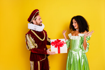 Young couple in elegant royal costumes bonding and exchanging a gift against a vibrant yellow...