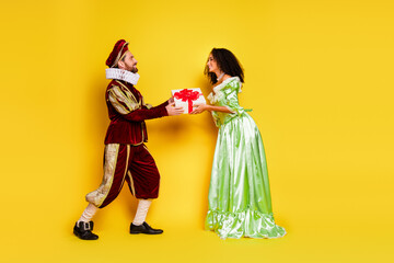 Couple in Elegant Historic Costumes Exchanging a Gift Against Bright Yellow Background