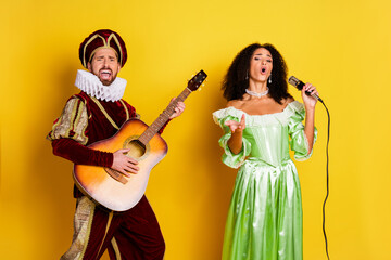 Elegant couple in regal costumes performing music, with vibrant expressions against a yellow...
