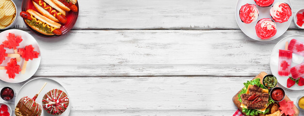 Canada Day patriotic food. Top view double border on a white wood banner background. Hot dogs, hamburgers and maple leaf red and white theme snacks. Copy space.