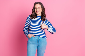 Charming mature woman wearing stylish striped sweater showing thumbs up sign against a vibrant pink background