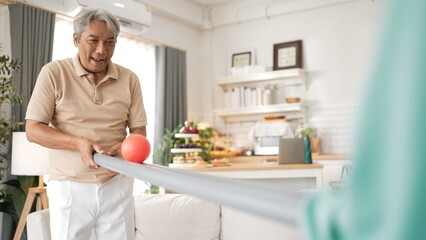 Elderly man playing a ball rolling game with his partner at home, practicing hand-eye coordination, focus, and motor skills for mental and physical wellness. Preventing healthcare concept. Myrmidon.