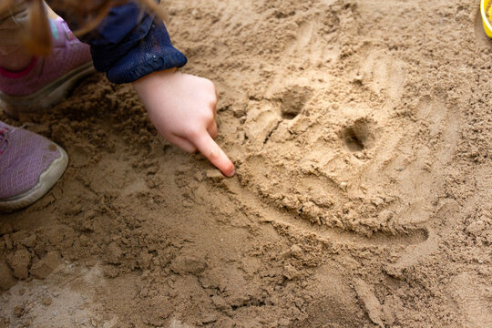 main d'enfant qui dessine un smiley sur le sable