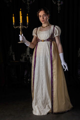 Fototapeta premium A Regency woman wearing evening attire, standing and holding a lit candelabra