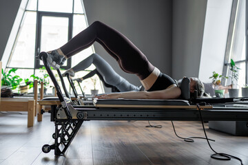 A group of woman exercises Glute bridge on a reformer bed machine in natural sunlight, focusing on pelvis and hips.