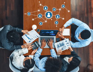 A top-down view of a diverse business team collaborating in a modern office, engaging in a data analysis and networking discussion using various technology and documents. Amity