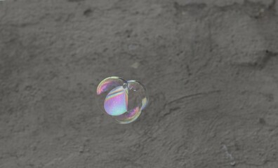 Una toma de cerca de una burbuja de jabón volando en el aire con una pared al  un fondo de color  gris.