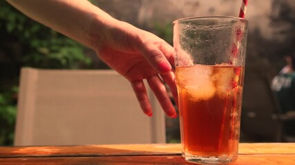 A hand reaches for a cold glass of iced lemon tea covered with condensation. The perfect refreshing summer drink to quench thirst in hot weather with bright citrus and cool moisture. - Powered by Adobe