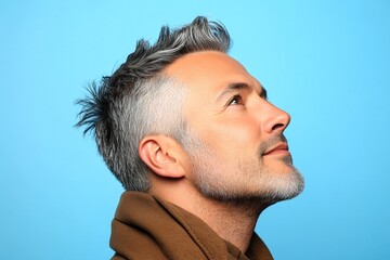 Obraz premium Idea concept art of style for aging men. Blue solid background. A happy man in a studio photo. Elegant men's layered waves haircut - midlife white man with grey hair.