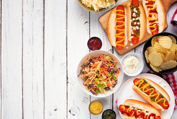 BBQ side border with hot dogs, classic salads and snacks. Above view table scene over a white wood background. Copy space.