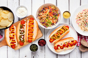 BBQ table scene with hot dogs, classic salads and snacks. Above view over a white wood background.