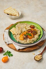 Appetizer, baked eggplant dip with yogurt on a green ceramic plate on a light concrete background. Served with cherry tomatoes, toasted bread and pine nuts. Recipes eggplant.
