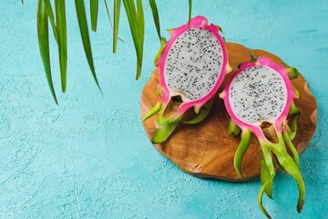 Fresh pink skinned pitahaya or dragon fruit cut in half on wooden board against turquoise concrete...