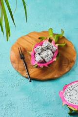 Cubed pitahaya or dragon fruit pulp in a bowl made of its peel on a wooden board on a turquoise...