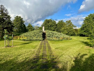 A wide green meadow stretches toward a lush tree line beneath a vibrant, cloud-filled sky. The open...