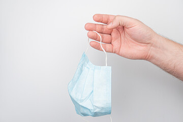 Light blue disposable surgical mask held by hand against neutral background, even indoor lighting.