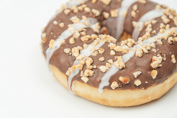 A single donut with glossy glaze, garnished with nuts or seeds, sits on a light surface against a blurred kitchen backdrop White icing drizzle is visible Bright lighting highlights textures