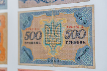 Historical, aged Ukrainian banknote pasted on a surface Features a portrait and intricate patterns in blues, greens, purples, and yellows Shows both left and right sides with 3D effect under natura