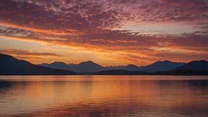 Fototapeta premium Vibrant Sunset Casts Warm Hues Over Tranquil Lake Surrounded by Majestic Mountains in the Evening Sky