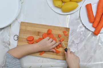 Safety-first cooking lesson: child uses blunt knife to chop steamed carrots. Ideal visual for...