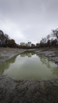 Empty lake with stagnant water and residential buildings under cloudy sky.