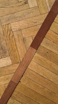 Old parquet flooring with classic herringbone pattern and a dark wooden strip.