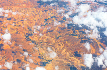 Arid landscape, sculpted by erosion, stretches beneath sky dotted with fluffy clouds. Aerial view...