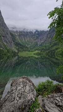 Crystal-clear Obersee Lake in Berchtesgaden National Park, surrounded by mountains and clouds. Peaceful, scenic view in the Bavarian Alps, Germany.